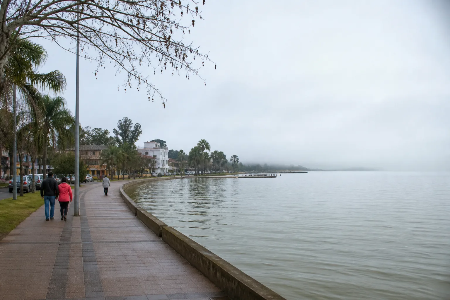 Orla invernal del lago Ypacaraí en San Bernardino, Paraguay, con niebla y gente abrigada — no es playa de verano